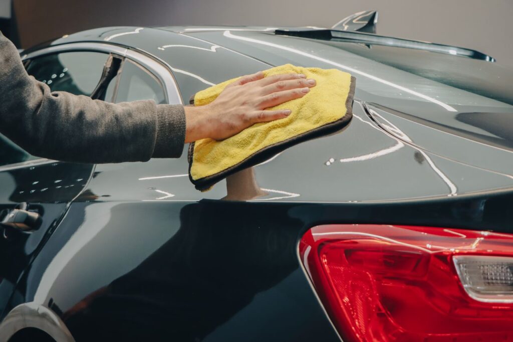 pexels photo 14615260 Close-up of hand polishing a shiny car with a yellow cloth indoors.
